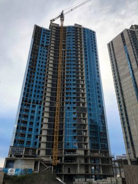 Mavi gökyüzüne karşı büyük bir vinç kullanarak beton ve cam ve gaz silikat blokların monolitik çerçeve ev, bina, gökdelen inşaatı