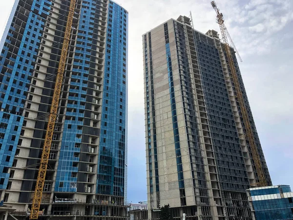 Construction of a monolithic frame house, building, skyscraper of concrete and glass and gas silicate blocks using a large crane against a blue sky