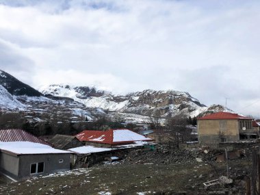 Küçük taş evler, yüksek dağ zirveleri sis ve mavi bir gökyüzüne karşı kayak için kayalar kaplı güzel bir dağ soğuk kış tesisi köyde binalar
