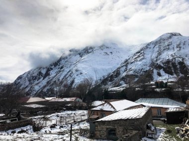 Küçük taş evler, yüksek dağ zirveleri sis ve mavi bir gökyüzüne karşı kayak için kayalar kaplı güzel bir dağ soğuk kış tesisi köyde binalar