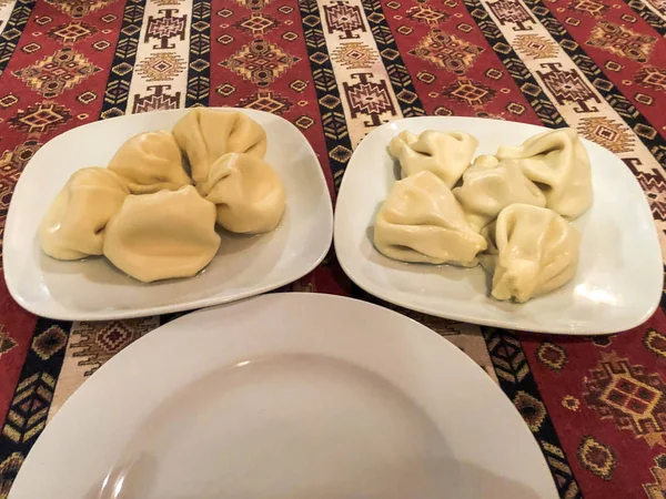 Due porzioni di nutriente gustoso khinkali, manti su piatti bianchi in ceramica sul tavolo nel ristorante nazionale georgiano sul tavolo con una tovaglia rossa — Foto Stock