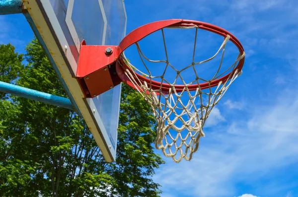 Red sports round basketball basket for playing basketball streetball on an open street area under the open sky with a net against a blue sky and trees