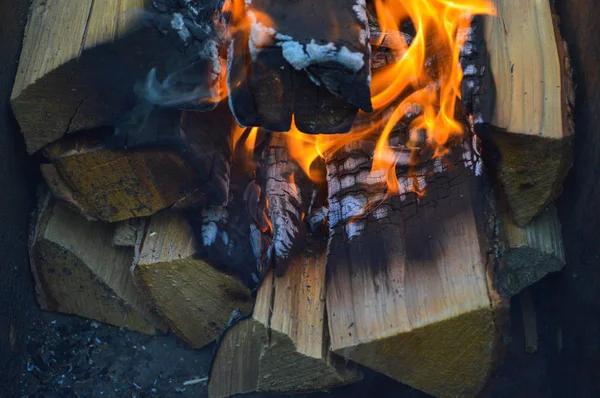 Madera quemando tablones carbonizados calientes de troncos de madera en un fuego con lenguas de fuego y humo. Textura, fondo —  Fotos de Stock