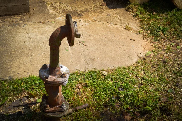 An iron rusty corrosive old industrial water supply pipe for water supply with a flange moving with nuts and studs sticks out of the ground of green grass — Stock Photo, Image