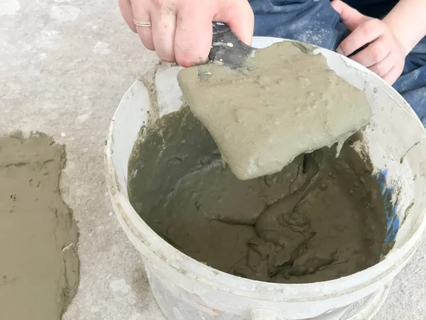 Büyük bir beyaz plastik inşaat kova sıva, kiremit tutkal, bir daire, ev, duvarlar tesviye ve dökme onarım ı için çimento bir metal spatula yoğuruyor ile Builder eller