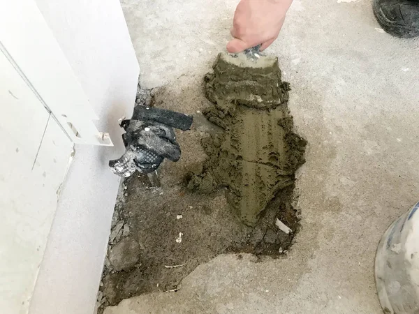 Builder hands with a metal spatula plaster the wall, pours the screed with plaster, tile glue, cement for the repair of the apartment, building a house, leveling the walls and pouring the screed