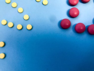 yuvarlak pembe ve sarı hapların hacmi harf biçiminde. Genel durumu korumak ve bağışıklık sistemini güçlendirmek için ilaçlar. Mavi renkli arka planda parıltısız ilaçlar