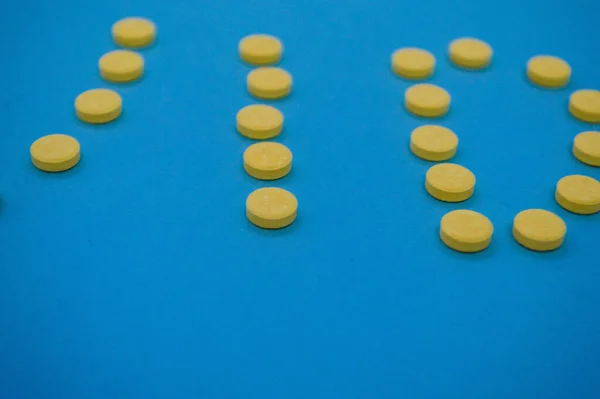 ボリュームのある黄色の錠剤が文字の形で青の背景に撃たれました。缶から注がれた医薬品は色のついた背景で上から撮影されます。英語のアルファベットを錠剤の形で — ストック写真