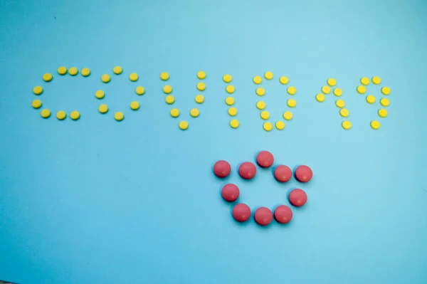 Többszínű tabletták volumetrikus felirata egy kék papíralapú koronavírusra. A korona rózsaszín domború tabletta a felirathoz. vírusfertőzések kezelésére szolgáló gyógyszerek — Stock Fotó