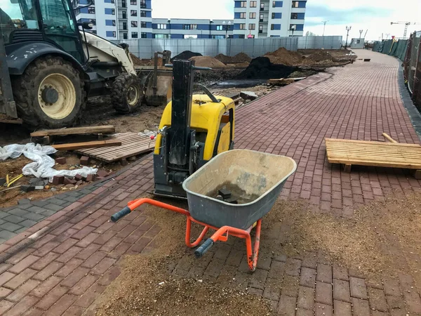 Trolley voor het transport van zware materialen, beton, bakstenen en zand. naast de machine voor de vervaardiging van wegdekken. tegen de achtergrond van de wielen van een rupstrekker — Stockfoto