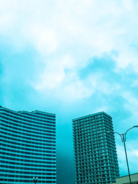 Um edifício alto e luminoso no centro da cidade. edifício residencial high-rise em branco contra um céu azul brilhante. perto de uma casa azul na forma de uma onda. novo bairro na cidade — Fotografia de Stock