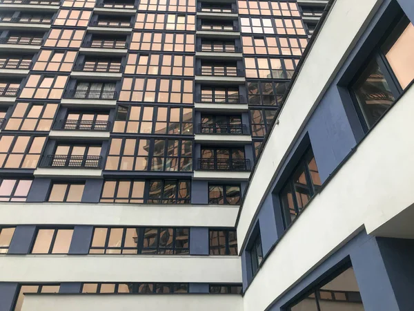 Wieżowiec mieszkalny wysoki budynek z oszronionymi oknami w centrum miasta. niebiesko-białe szklane ściany z przejściem do innego budynku. przymrożone okna z niezwykłym efektem lustra — Zdjęcie stockowe