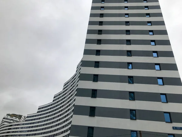 Tall residential building, skyscraper in the form of a wave. from the side, the house is blue and white. many small glass windows around the perimeter. skyscraper on the background of the cloudy sky — Stock Photo, Image