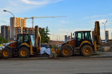 Şehir merkezinde inşaat makineleri inşa ediliyor. Kum kazmak ve temel yapmak için kazıcılar. Şehirde yeni bir çeyrek oluşturmak için sarı büyük inşaat ekipmanları.