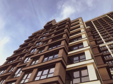 Şehirdeki insanların hayatları için şık bir apartman. Şehir merkezinde uzun, kahverengi ve beyaz bir bina. Gökyüzüne karşı panoramik pencereli bir ev. Konforlu ve modern bina