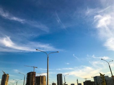 Yeni bir bölgenin inşaatı. Vinçler ağır beton bloklar taşıyor. Uzakta, yolu aydınlatmak için ışık görünür. Panoramik cilalı evler ve bireyselleştirilmiş tablolar