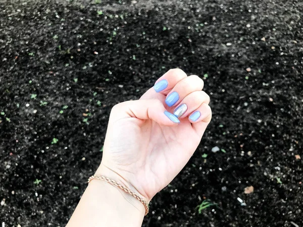 Clavos de plata azul brillante y brillante en la mano de la chica. filmado sobre un fondo de tierra negra. tierra fértil, mano de jardinero. hermosa manicura entre el suelo negro — Foto de Stock