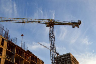 Beton bloklardan yeni bir konut inşaatı. Vinç yeni bir zemin inşa eder, blokları çeker. Metal çiviler beton bloklardan çıkmıştır. İkinci vinç yakınlarda bir ev inşa ediyor.