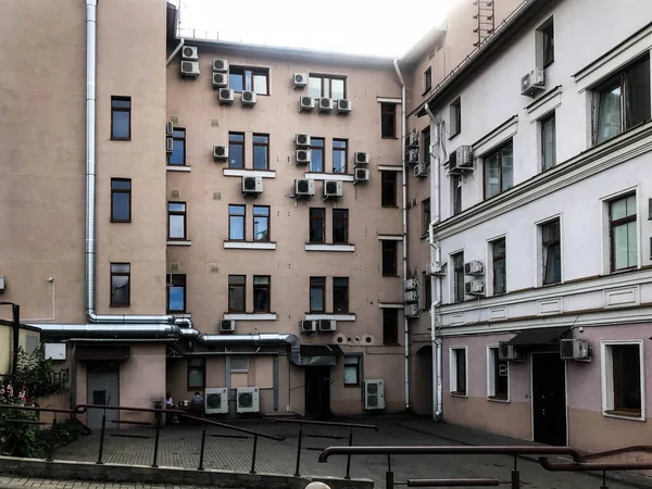 An orange house stands in the city, with many white air conditioners hanging from the windows. there is another house nearby. a pipe for draining water into the sewer hangs on the side — Stock Photo, Image