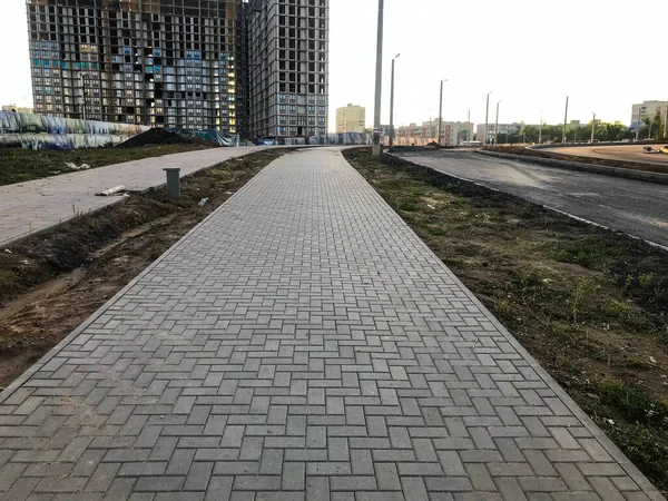 an asphalt block road leads to a new building complex in the city center. next to it there are concrete houses without painting yet. creating a comfortable and accessible environment for residents