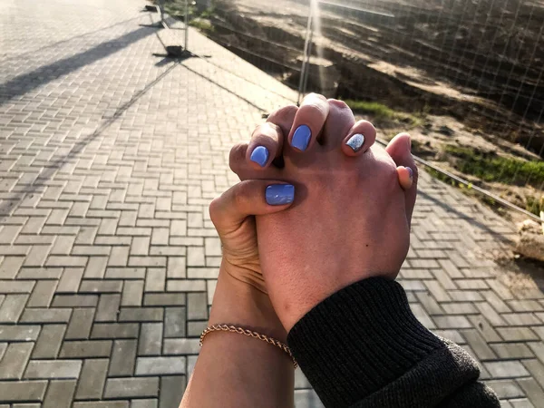 Κορίτσι και άντρας κρατιούνται χέρι-χέρι. Τα νύχια του κοριτσιού είναι καλυμμένα με μπλε-ασημί βερνίκι. όμορφο και κομψό μανικιούρ. αγάπη μεταξύ ενός άντρα και μιας γυναίκας. με φόντο την άσφαλτο — Φωτογραφία Αρχείου
