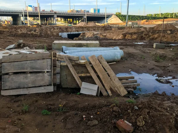 Chantier de construction, flaques de sable et de boue. il y a des structures en bois sur le site. sur le fond du pont, carrefour routier. tuyaux et matériaux de construction reposent sur le sol — Photo