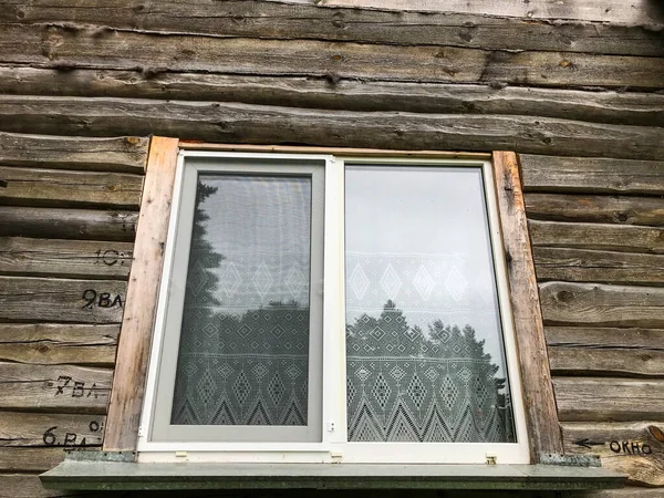창문은 틀에 나무로 되어 있습니다. 마을에 있는 목조 건물. 나무 틀이 있는 유리 창문. 창문에는 커튼이 걸려 있고 얇은 종이로 만든 툴레는 — 스톡 사진