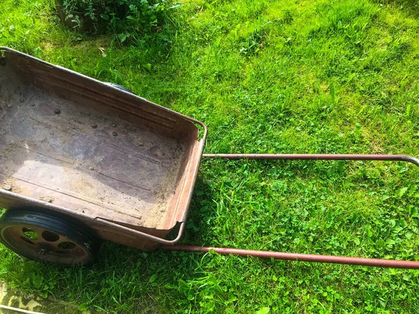 Une brouette métallique pour le transport de produits et d'engrais se trouve sur l'herbe verte. une brouette pour les travaux de jardin. jardinier, inventaire jardinier. soins de jardin — Photo