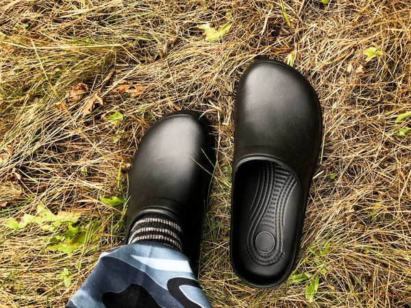 black rubber overshoes are worn on one leg. shoes on dry grass. autumn walk through the forest. wet grass after rain. protection of feet and socks from wet and cold ground