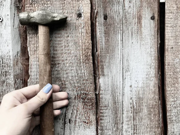 hammer on a wooden handle with a metal end. girl with blue manicure hammer nails into a wooden fence. stylish nails, trendy manicure. carpenter woman