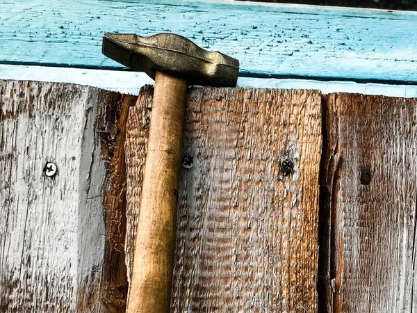 Marteau sur une poignée en bois avec une extrémité en métal. le marteau est suspendu à une clôture en bois, enduite de peinture bleue. outils pour construire et faire une clôture, maison. marteler dans les ongles — Photo