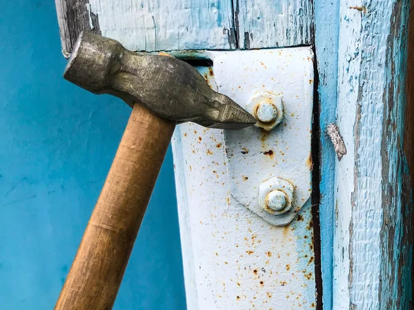 Marteau sur une poignée en bois avec une extrémité en métal. clouer des clous dans une surface métallique. tôle est peinte en gris. sur un fond de bois bleu — Photo