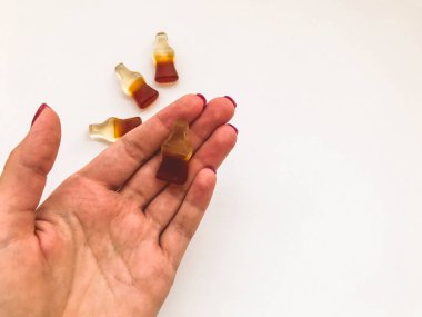 Marmelatlı şekerler. Kırmızı manikürlü bir kızın elinde bir şişe limonata şeklinde şekerler yatıyor. Çocuklar için lezzetli, çiğnenmiş bir tatlı. Jelibon.