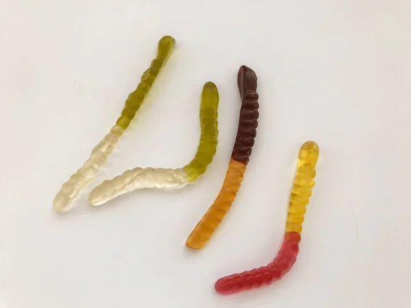 Мармеладные черви. желатиновые черви, разноцветные. бело-зеленый и желто-коричневый черви ползают вместе на белом матовом фоне — стоковое фото