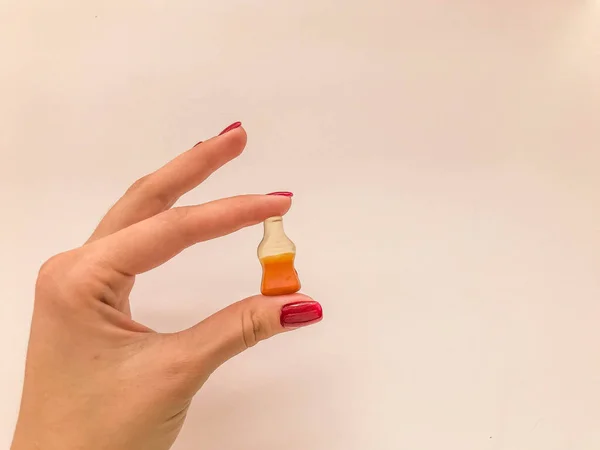 Dulces de mermelada. una chica con una manicura roja sostiene dulces en forma de botella con limonada. caramelo dulce en forma de una botella de cola, caramelo gomoso — Foto de Stock