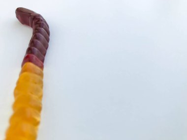 Jelibon solucanları beyaz bir arka planda yatar. Parlak, ağız sulandıran, kahverengimsi sarı renkli jöle solucanlar. Ağız sulandırıcı tatlılar. Cadılar bayramında çocukları tedavi etmek