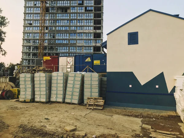 Nuovo edificio parzialmente senza finestre. accanto a una piccola, luminosa, colorata casa con disegni verdi, comunicazioni e un pannello elettrico. materiali da costruzione nelle vicinanze sono accatastati — Foto Stock