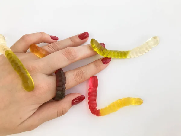 long, mouth-watering, multi-colored worms lie on the girl\'s hand with a bright red manicure. green, yellow, brown and transparent candy worms crawl along the hand