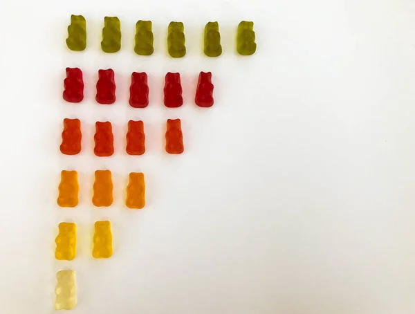 gummy bears lie on a white matte background. gummy bears are arranged in colors from dark green to transparent. the graph is decreasing. visual statistics with the image of sweets