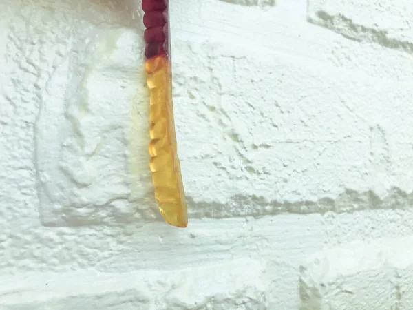 Липкий червяк на фоне белой кирпичной штукатурки стены. аппетитные желатиновые конфеты. черви на Хэллоуин. вкусные и сладкие мармеладки — стоковое фото