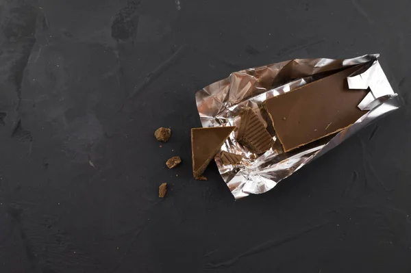Chocolate in foil packaging. Piece of chocolate. Dark background