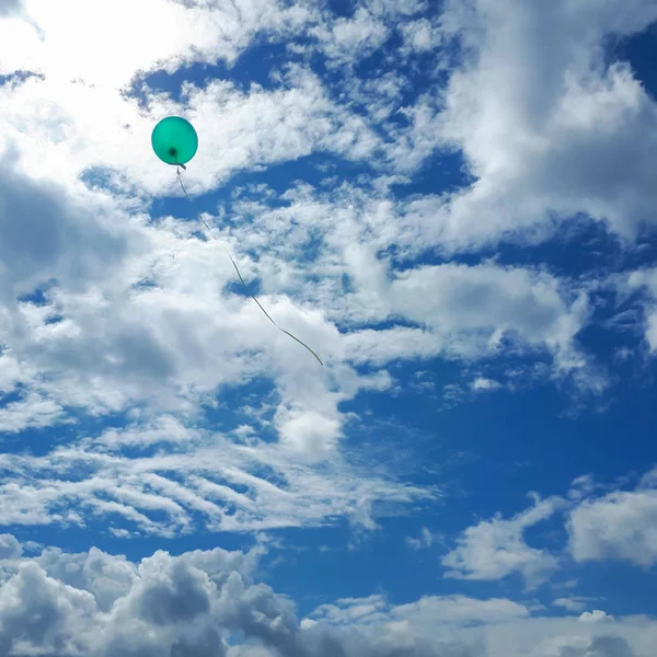 Green balloon flies into the clouds. Blue sky with feathery clouds