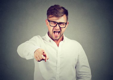Casual man in glasses and white shirt pointing at camera and screaming in blame and accuse clipart
