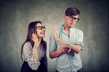 Annoying woman trying to distract young handsome man ignoring her while using a smartphone browsing internet. Phone addiction concept. clipart