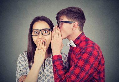 Gri arka plan üzerinde dururken şok arayan kadına sırrı söylemek gözlüklü genç adam