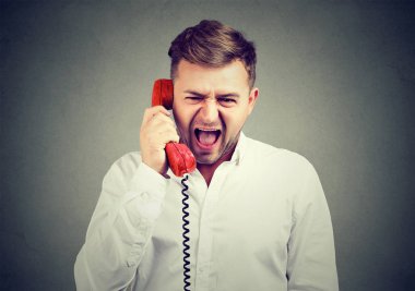 Kırmızı telefon cep telefonu tutarak ve gri arka plan üzerinde hayal kırıklığı içinde çığlık Beyaz tişörtlü genç adam. 