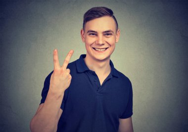 Parlak gülümsüyor ve gri arka plan üzerinde kameraya bakarken v işaret gösteren genç casual adam