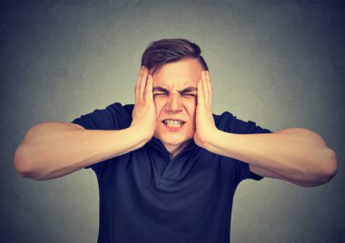 Acı ağrı ve stres ve gri arka plan üzerinde ellerini kafasına sıkma genç adam