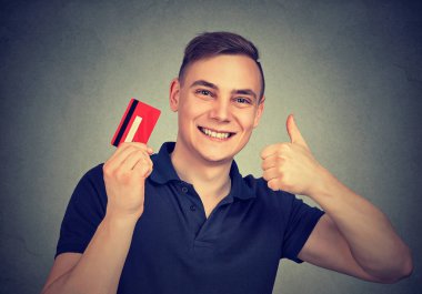 Genç adam holding kredi kartı gülümseyen ve gösterilen büyük tarifesi başparmak