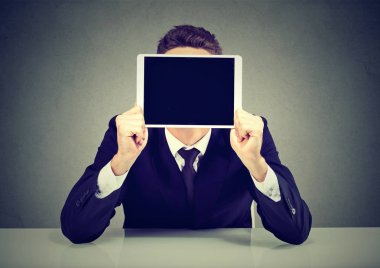 Tablet gri arka plan üzerinde oturan yüz önünde tutan takım elbiseli anonim işadamı